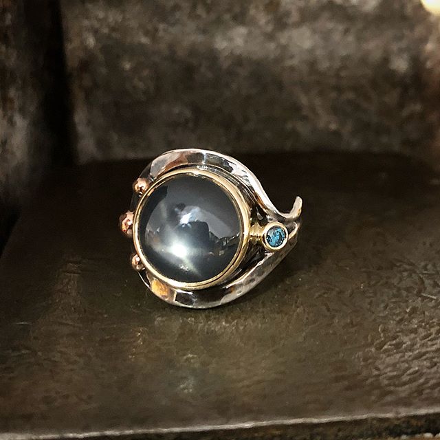 Ok here’s the one I was setting the other day. Australian star sapphire. It looks a steely grey but in natural light is shows a teal colour and several stars. I thought the little treated blue diamond was a nice little highlight. Hard to capture in the photos but this sapphire is mesmerising!!! Set in yellow and rose golds with a sterling silver band. Tool marked and oxidised. Almost ready to find a special home. POA